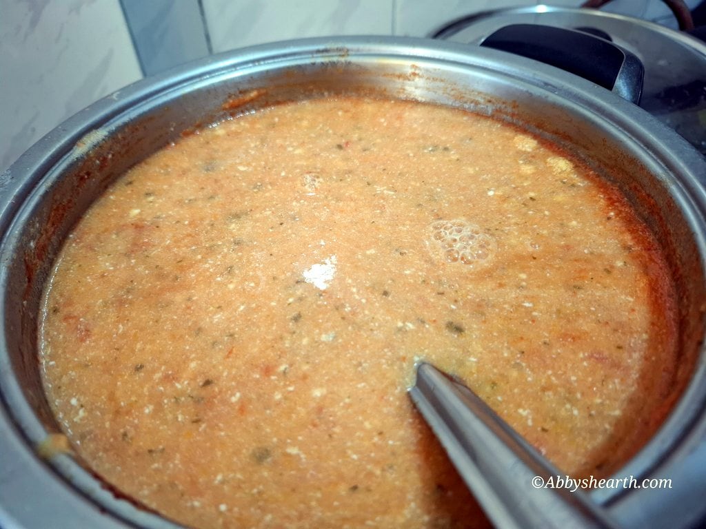 Homemade tomato carrot soup in a pot with cream just added to it with a ladle, ready to serve.