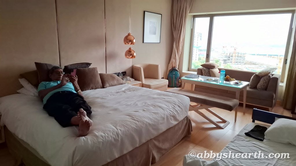 Man relaxing on bed in a hotel room with large window and city view.