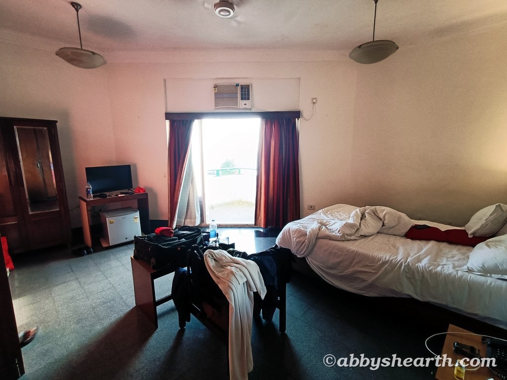 Hotel room with bed, TV, and balcony door in Mumbai, India.