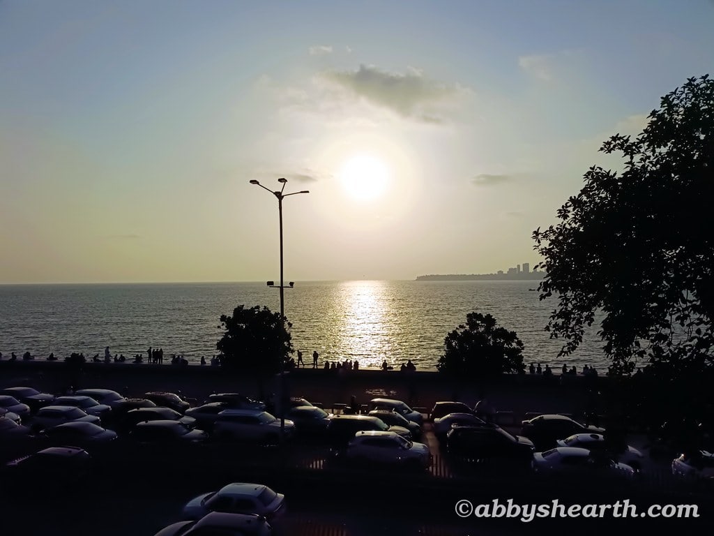 Sunset over the Mumbai coastline with cars and trees in foreground.