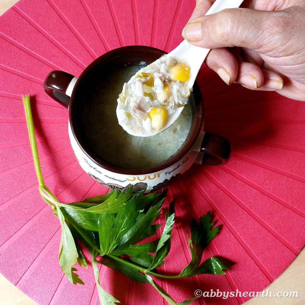 Hand holding a spoon of sweetcorn chicken and celery soup over a pot of soup.