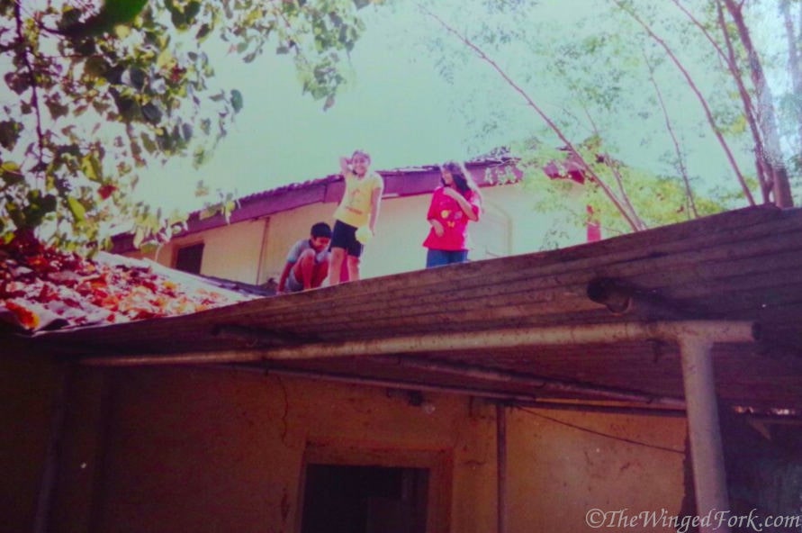 Three kids playing on the roof of an old bungalow.