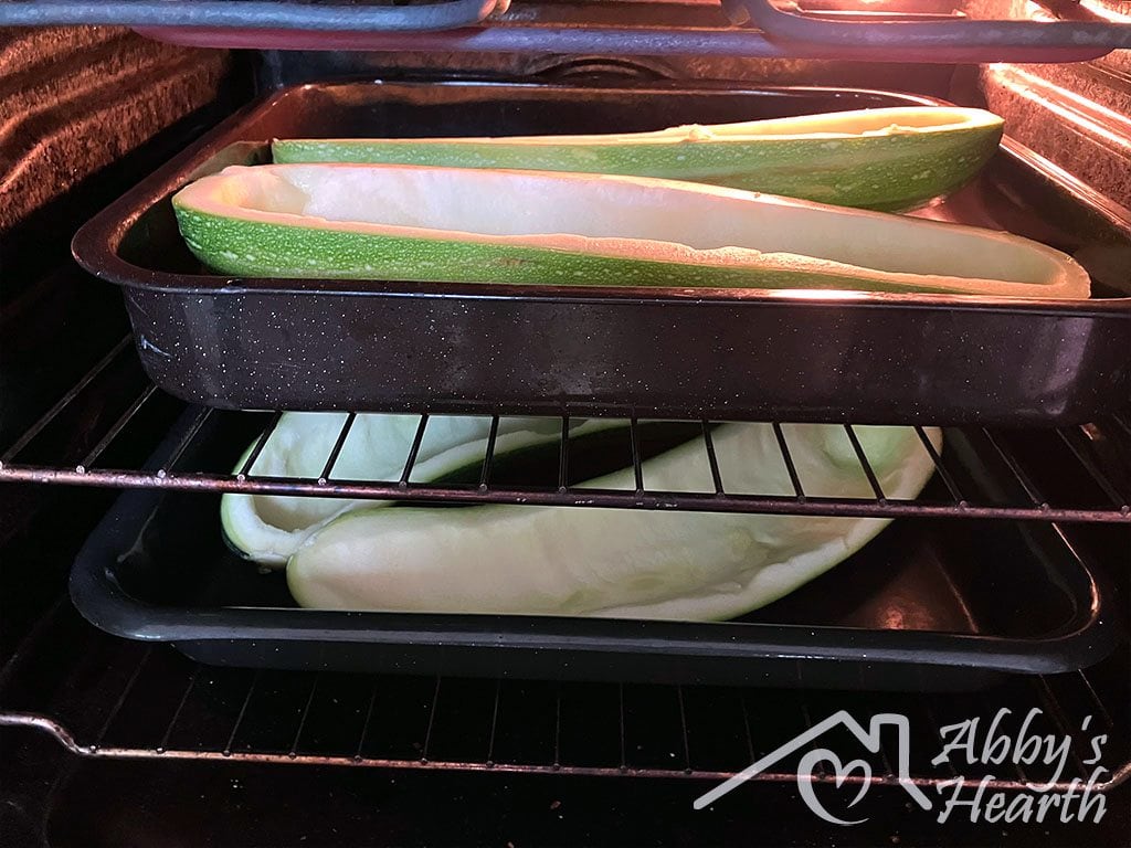 Hollowed out zucchini shells pre-baking in the oven on two trays.