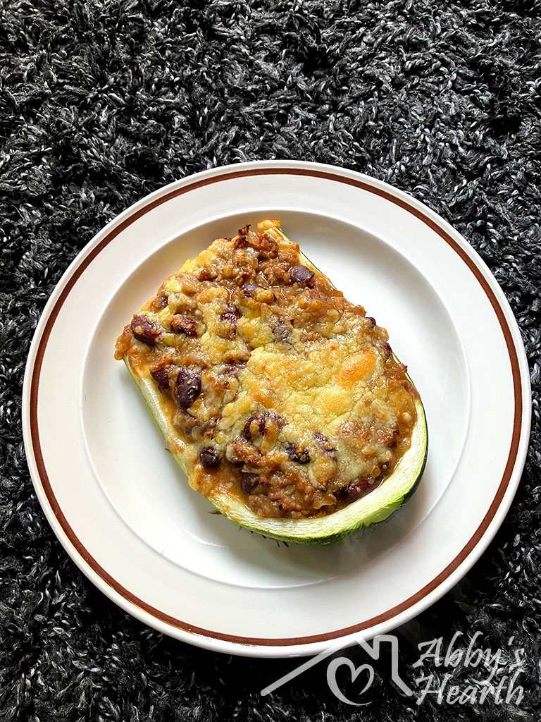 A baked zucchini boat filled with beef mince, kidney beans and golden melted cheese, served on a white plate.