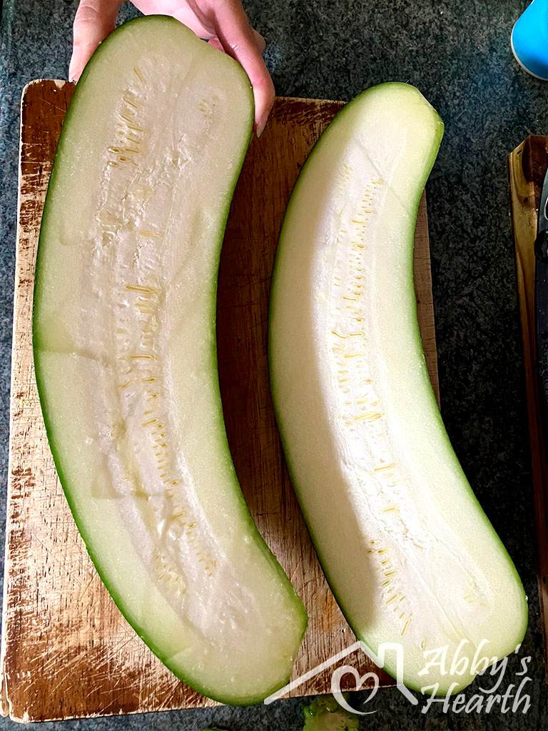Two curved zucchini halves cut lengthwise on a wooden chopping board.