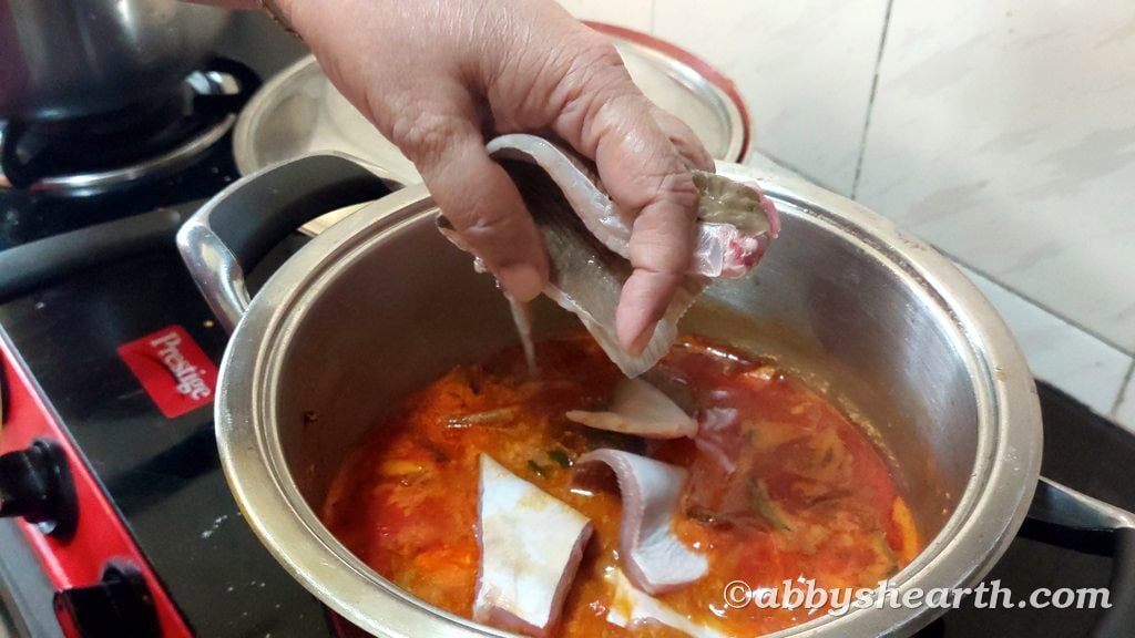Hand adding pakat/skate fish pieces to boiling curry.