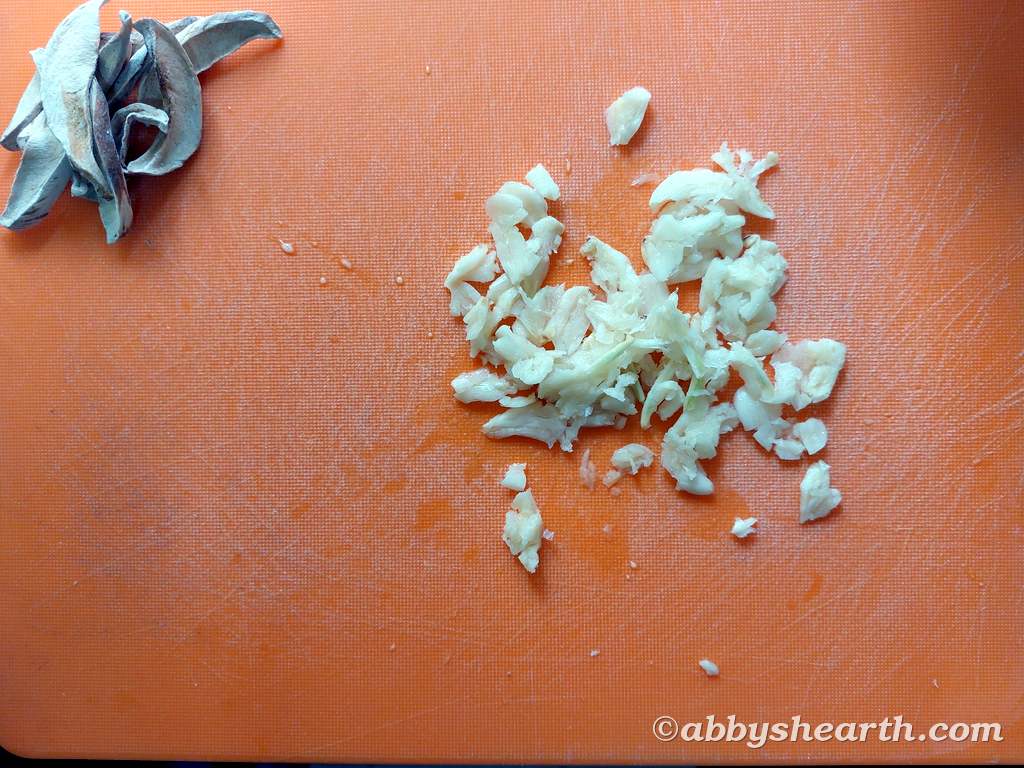 Crushed garlic on a chopping board next to amboshi (sundried mango).