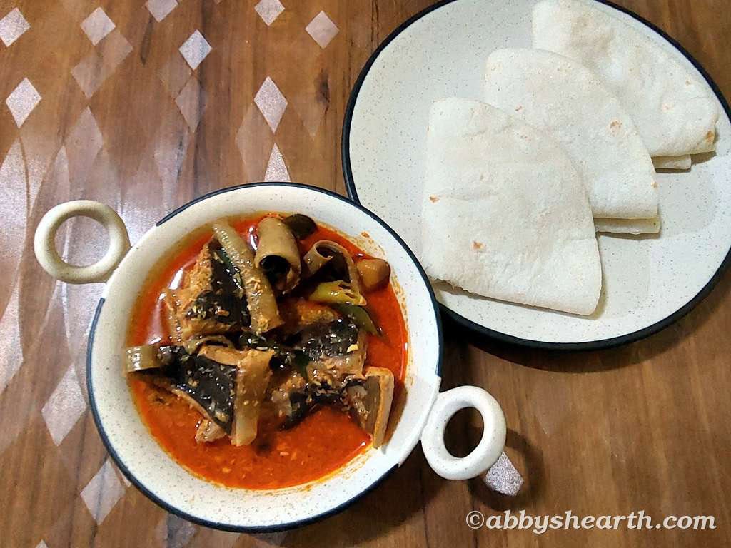 Top view of Pakat Lonvas curry in a pot next to a plate of apas/handbreads.