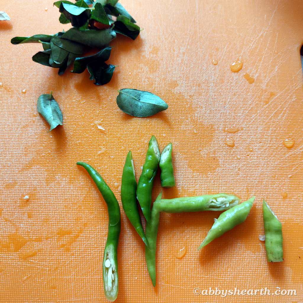 Green chilies slit diagonally next to curry leaves.