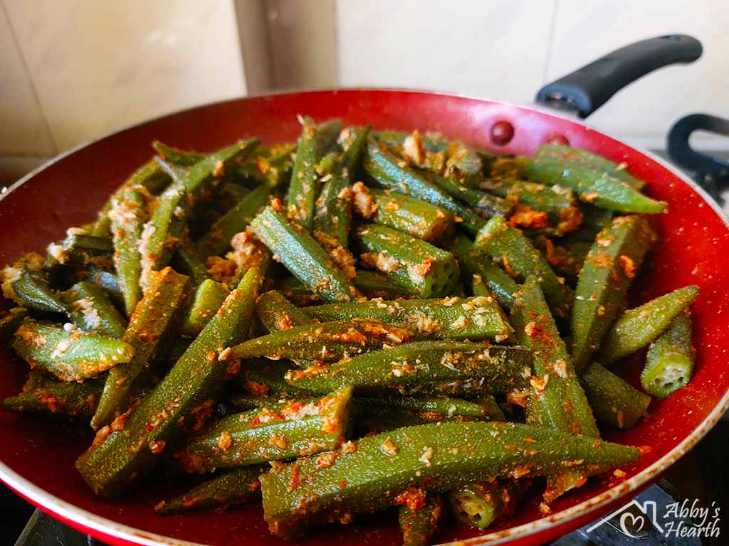 Semi-fried bhendi cooking in a frying pan.