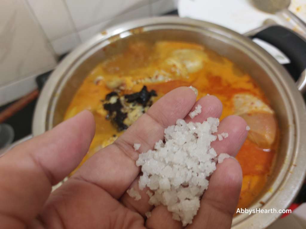 Hand holding sea salt over a pot of curry.