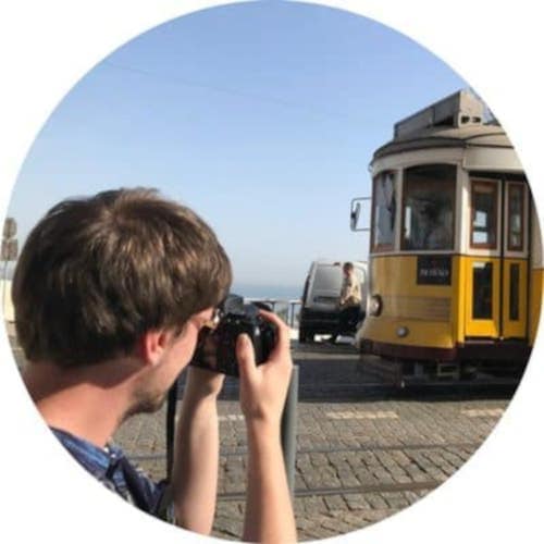 A boy holding a camera and pointing at a tram.