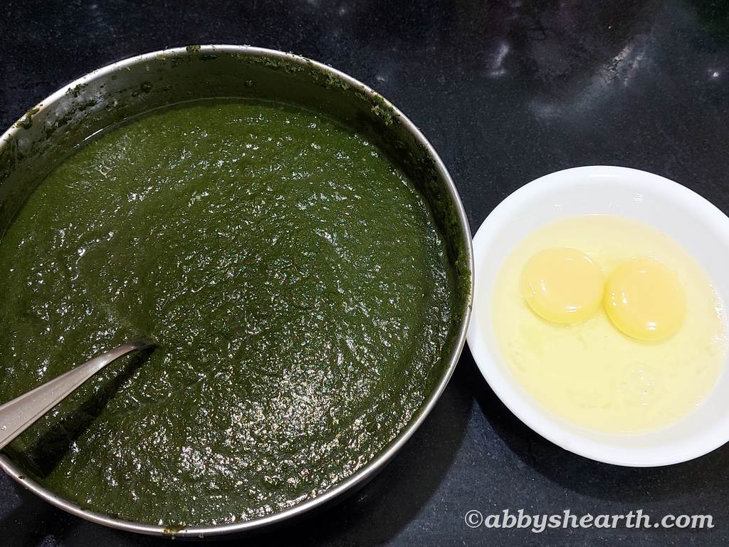 Homemade green chutney in a steel dish next to a bowl with 2 eggs.