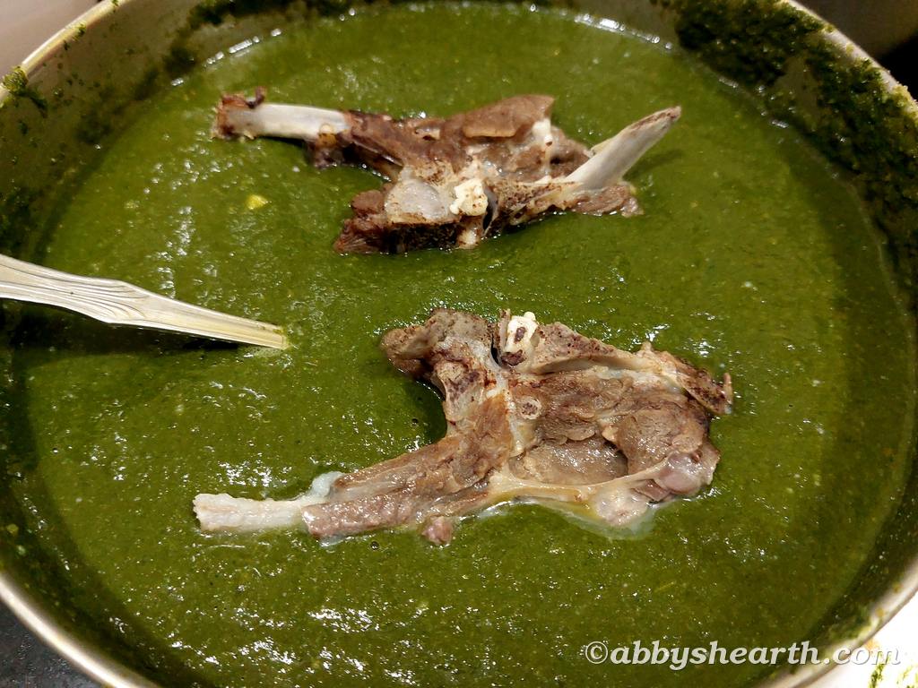 Mutton chops added to a pot of green chutney.