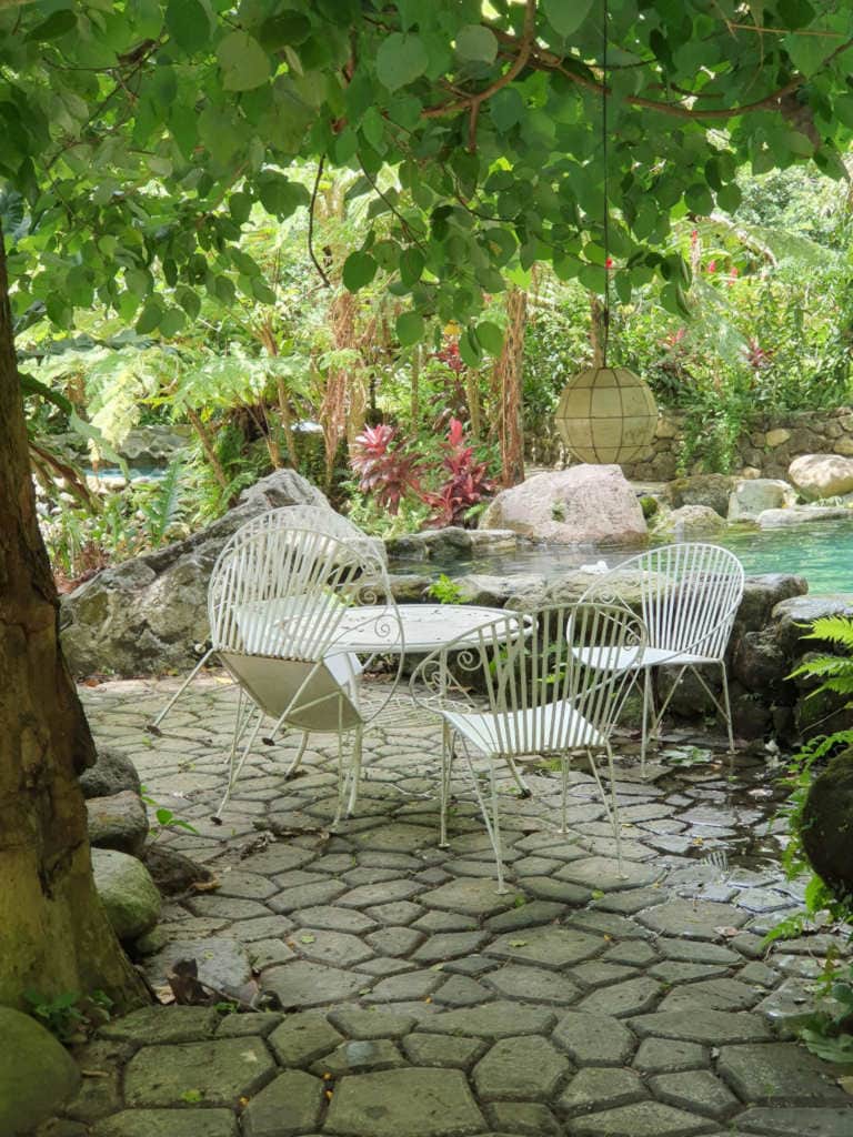 White table and chairs near a pool in a garden.