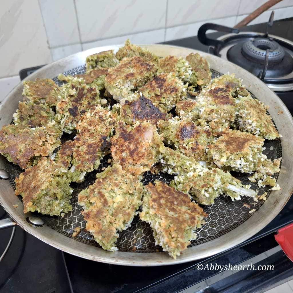 Green mutton chops coated with panko crumbs in a frying pan.
