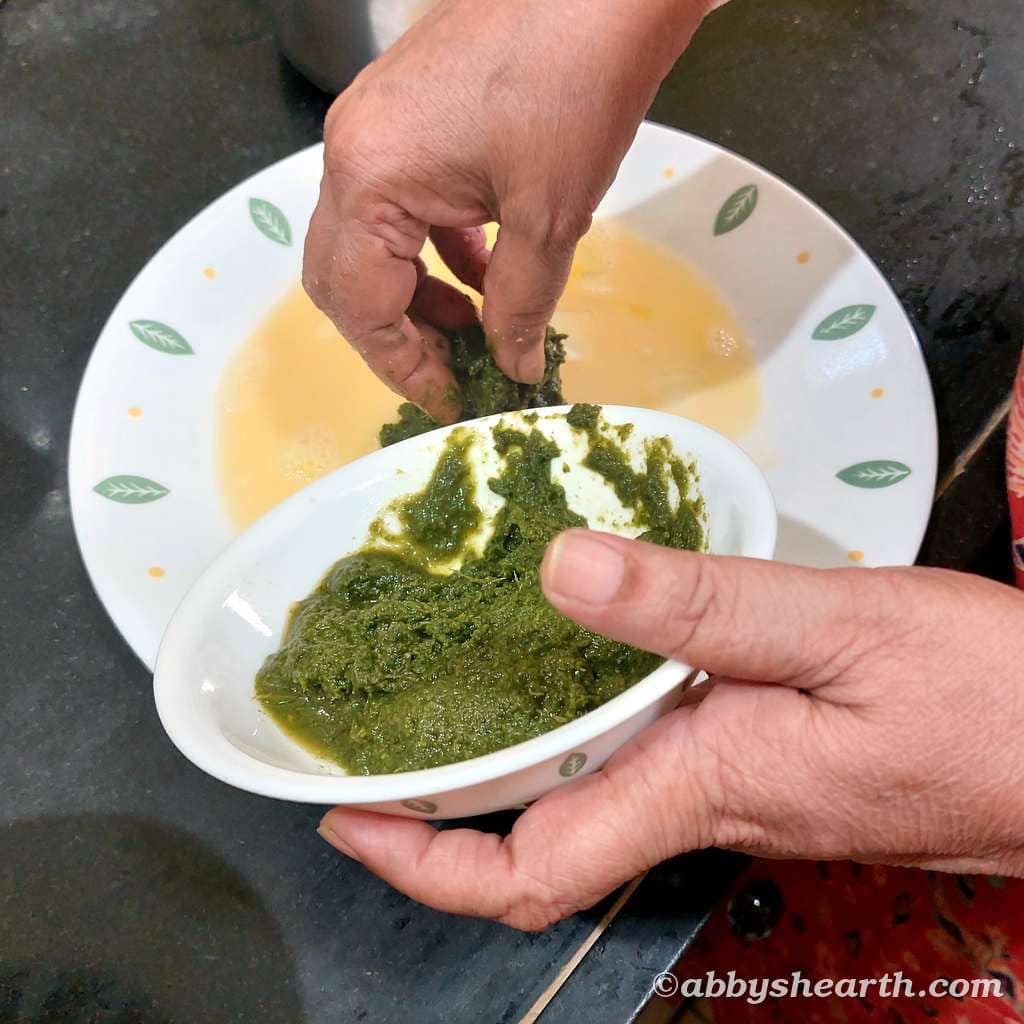 Hand adding green masala to a plate of beaten eggs.