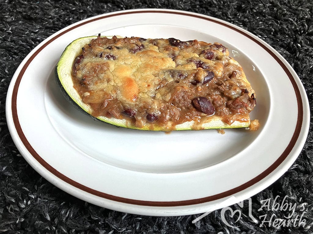 A baked zucchini boat filled with beef mince, kidney beans and golden melted cheese, served on a white plate.