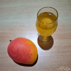 Glass of mango wine and ripe mango placed on the table.