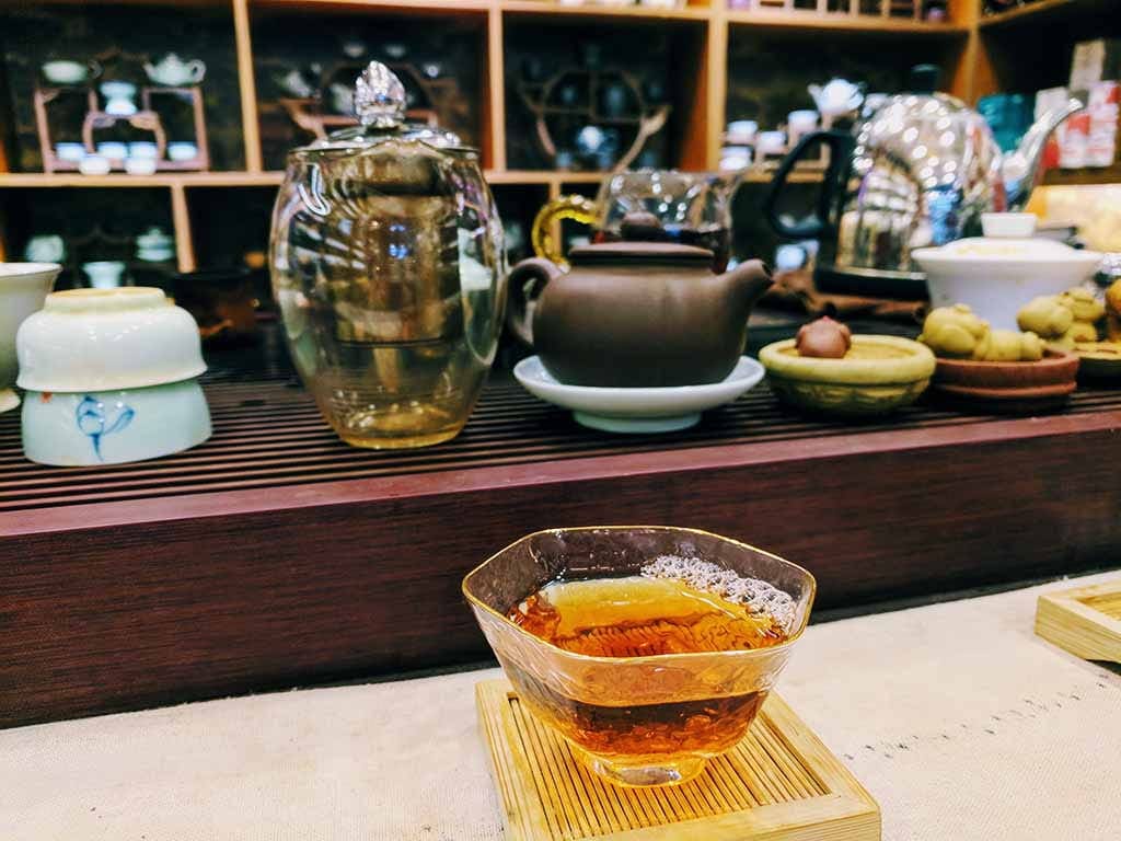 A glass of Chinese tea in front of different pots of tea.