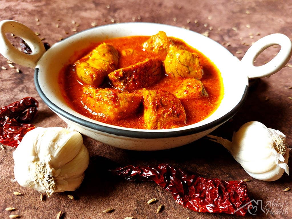 Roe vindaloo served in a ceramic kadhai with whole garlic and chillies at the side.