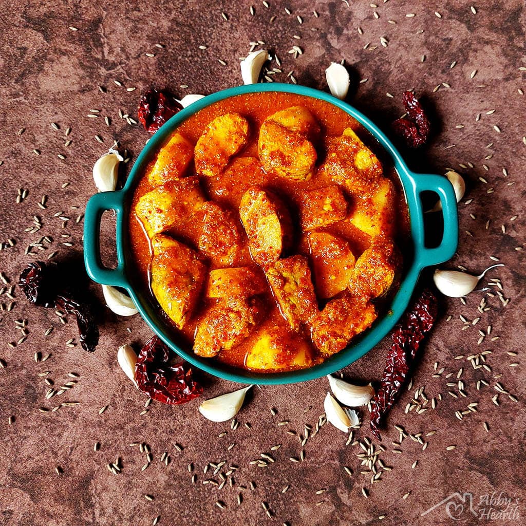 Roe vindaloo served in a green ceramic plate with whole garlic and chillies for decoration.