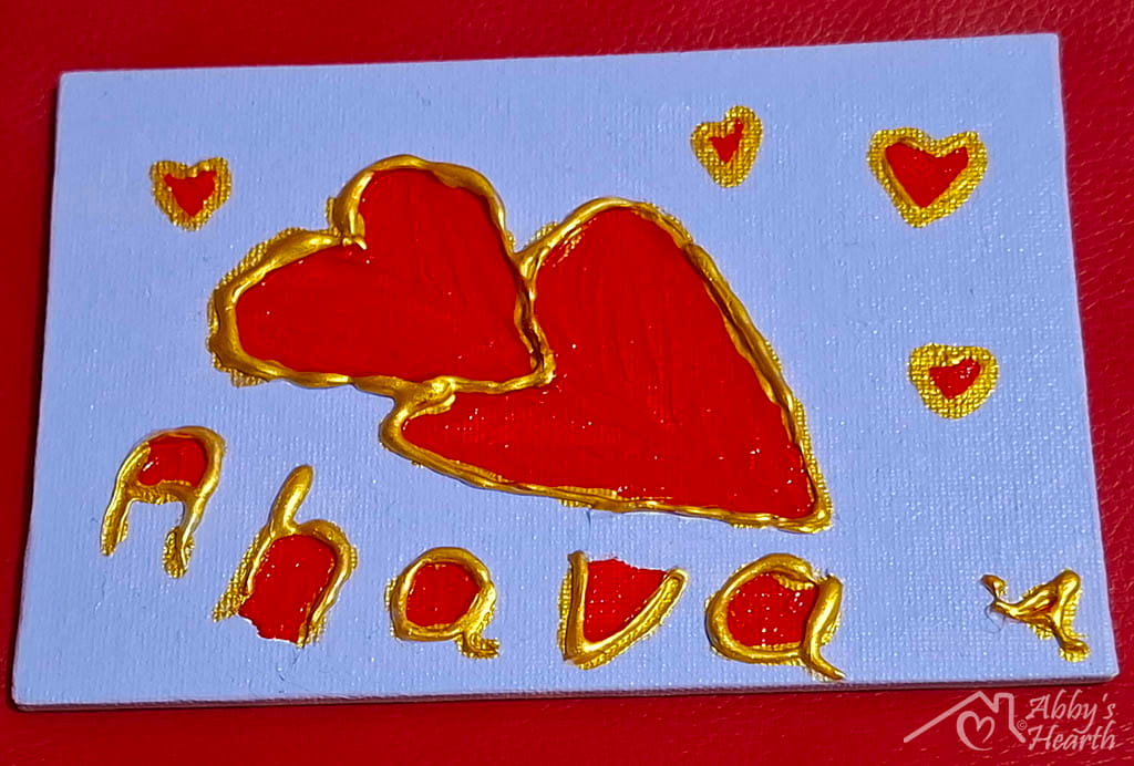 Glue art of Ahava love hearts in red and golden on lavender colour canvas.