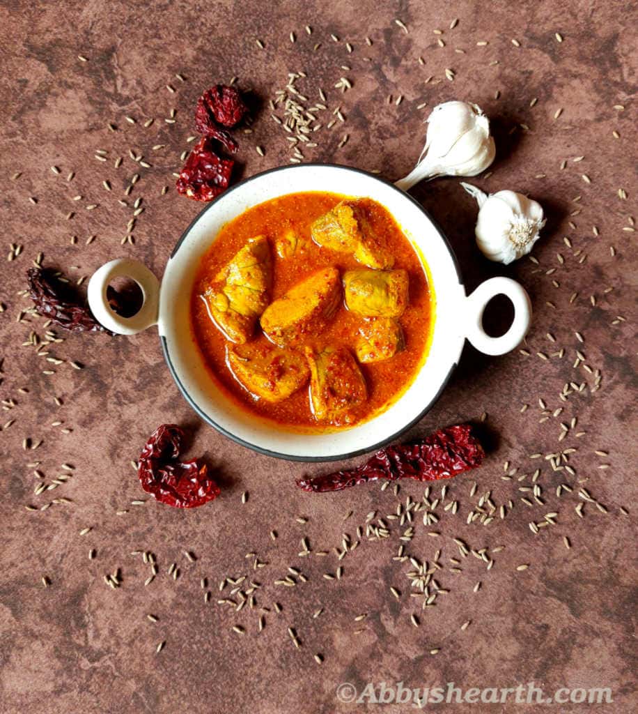 Roe vindaloo curry in a white dish surrounded by chillies, garlic and cumin.