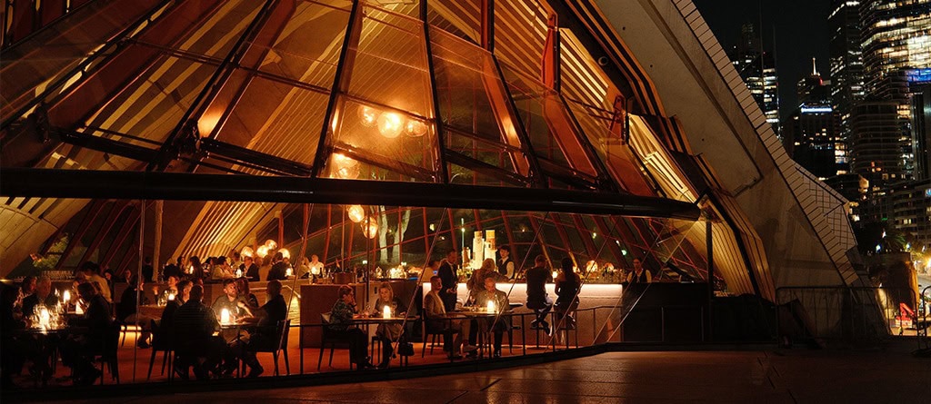 Diners seated at lit tables at the Bennelong Restaurant inside the Sydney Opera House.