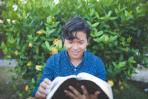 Boy reading an open Bible and smiling.