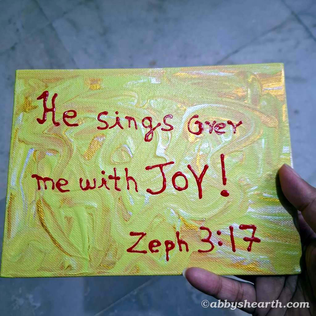 "God sings over me with joy" pink text on green and gold background.