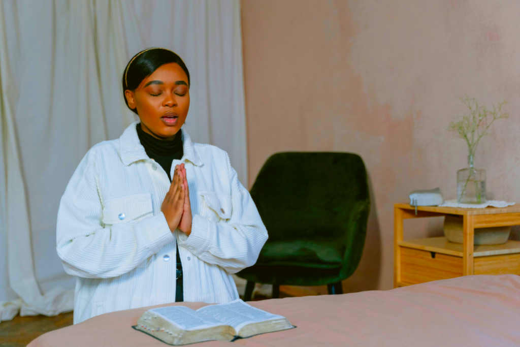 Lady kneeling near bed with bible praying.