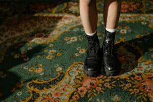 Legs with black boots on a green floral carpet.