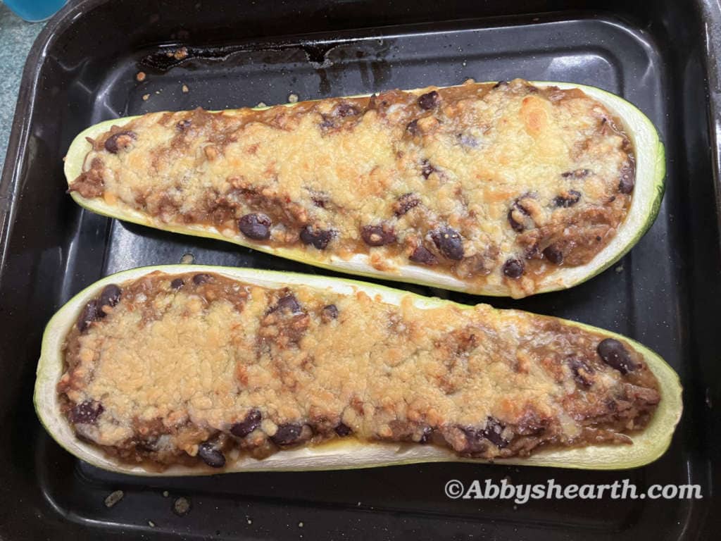 Two zucchini boats filled with beef mince, kidney beans and melted cheese, fresh from the oven in a baking tray.