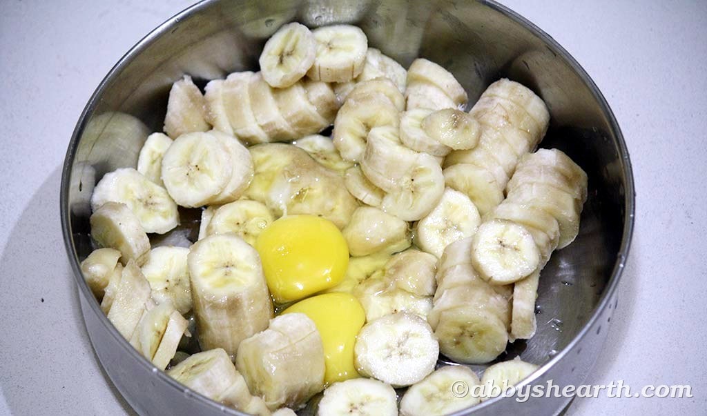Sliced overripe bananas and two eggs in a steel mixing bowl.