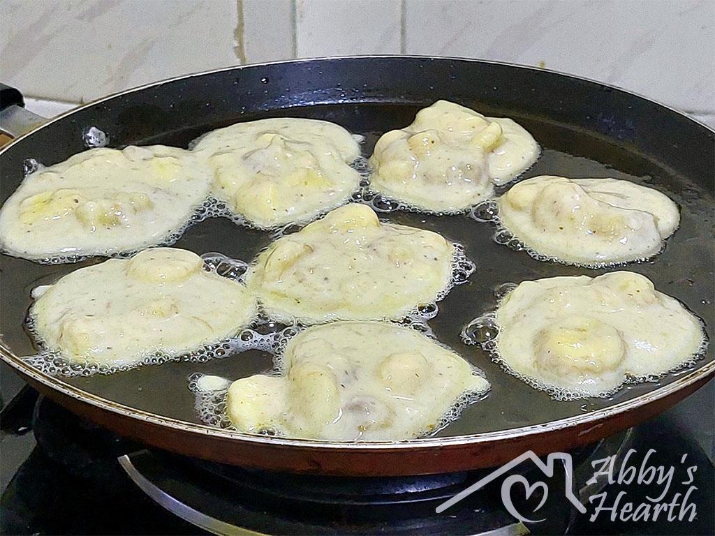 Banana fritter batter added to a frying pan in bits of 2 tablespoons.