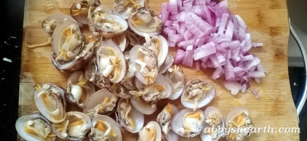 Opened cockle halves and diced onions ready on a chopping board.