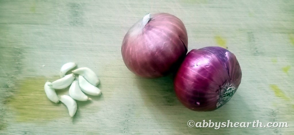 Two onions and seven garlic on a chopping board.