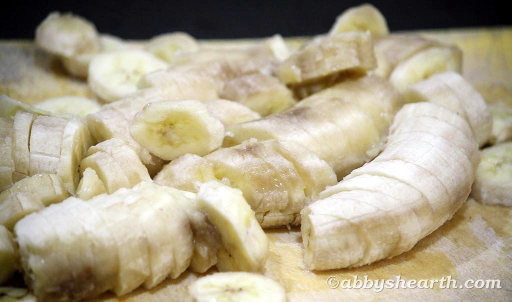 Sliced overripe bananas on a wooden chopping board.