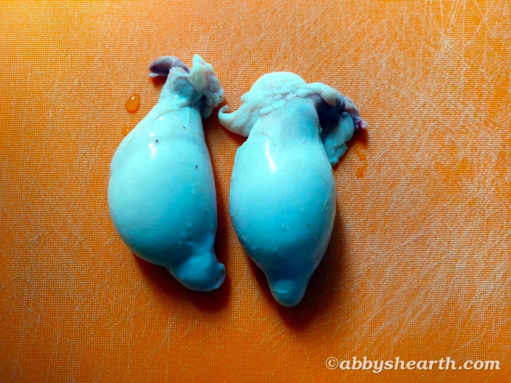 Two goat testicles on a chopping board.