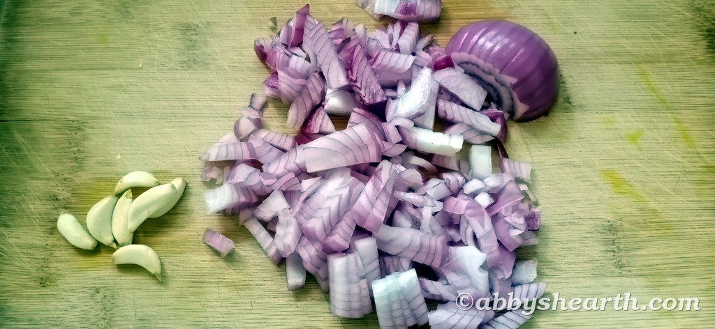 Diced onions and whole garlic on a chopping board.