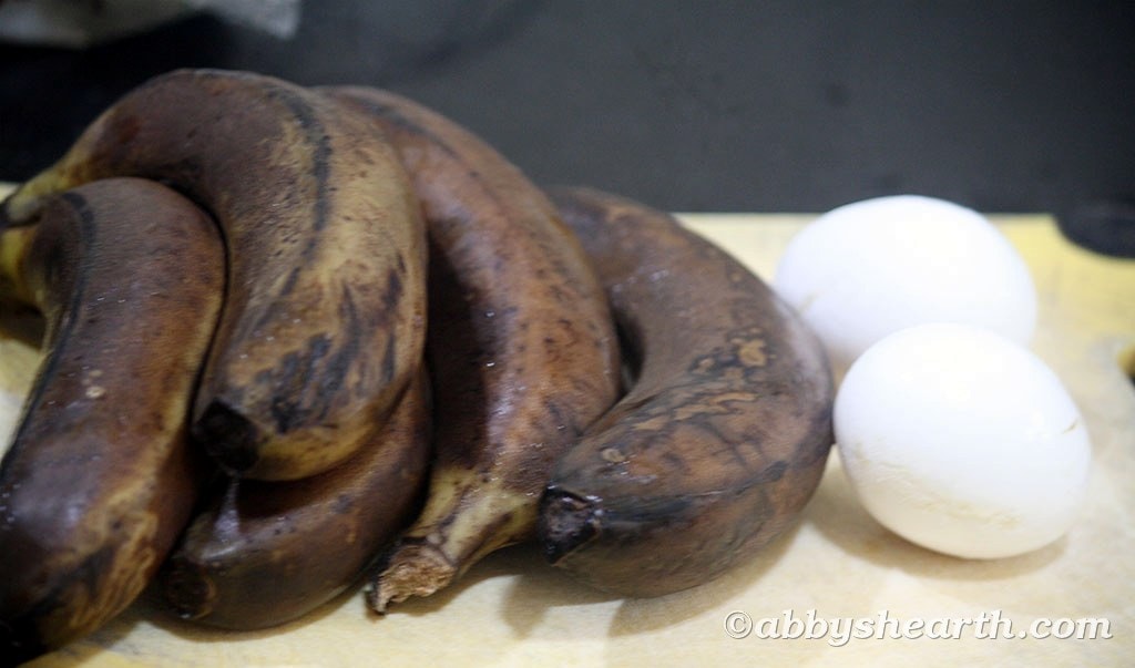 Very ripe, almost black bananas and two eggs on a chopping board.