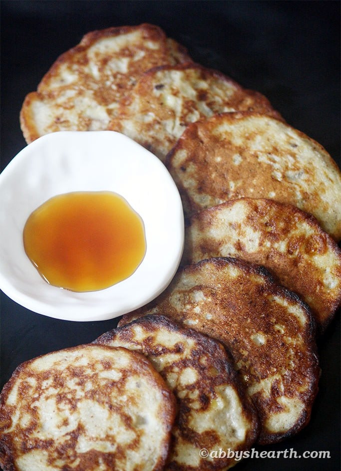 Sugar-free banana fritters arranged on a dark plate with a small bowl of honey.