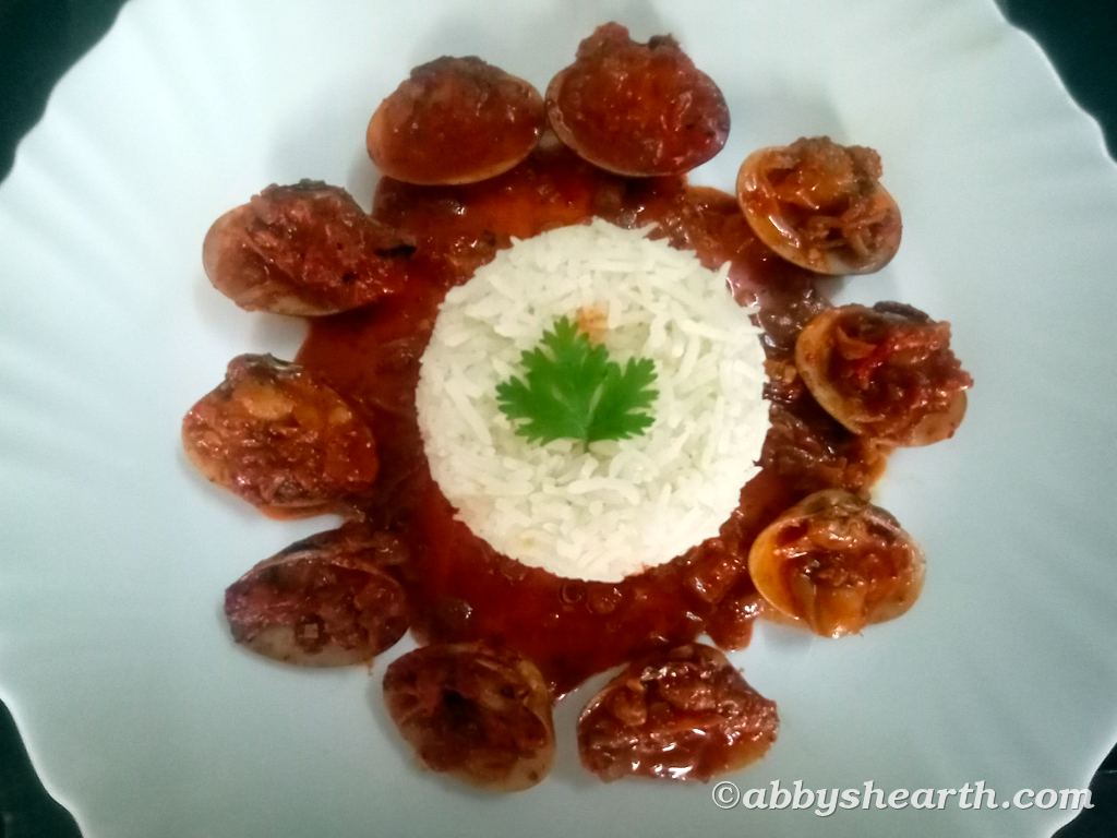 A mound of rice on a plate surrounded with thisra shells in a spicy gravy.