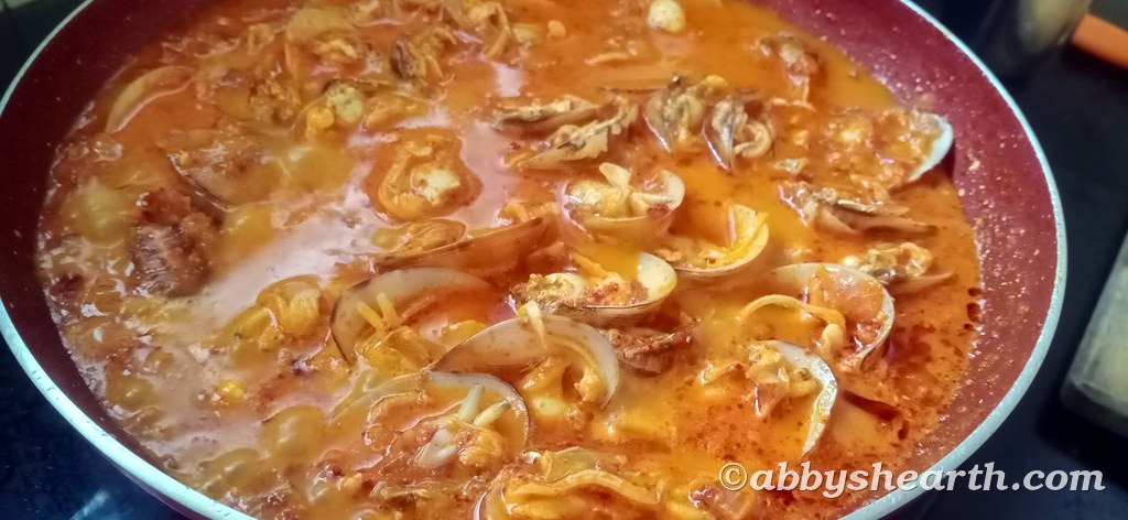 The cooked cockles in a spicy gravy in a red pan.