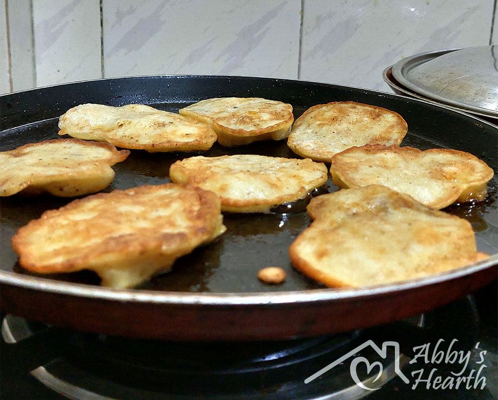 Banana fritters turned over in a frying pan.