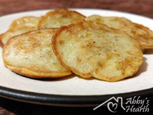 Six hot banana fritters in a beige plate.