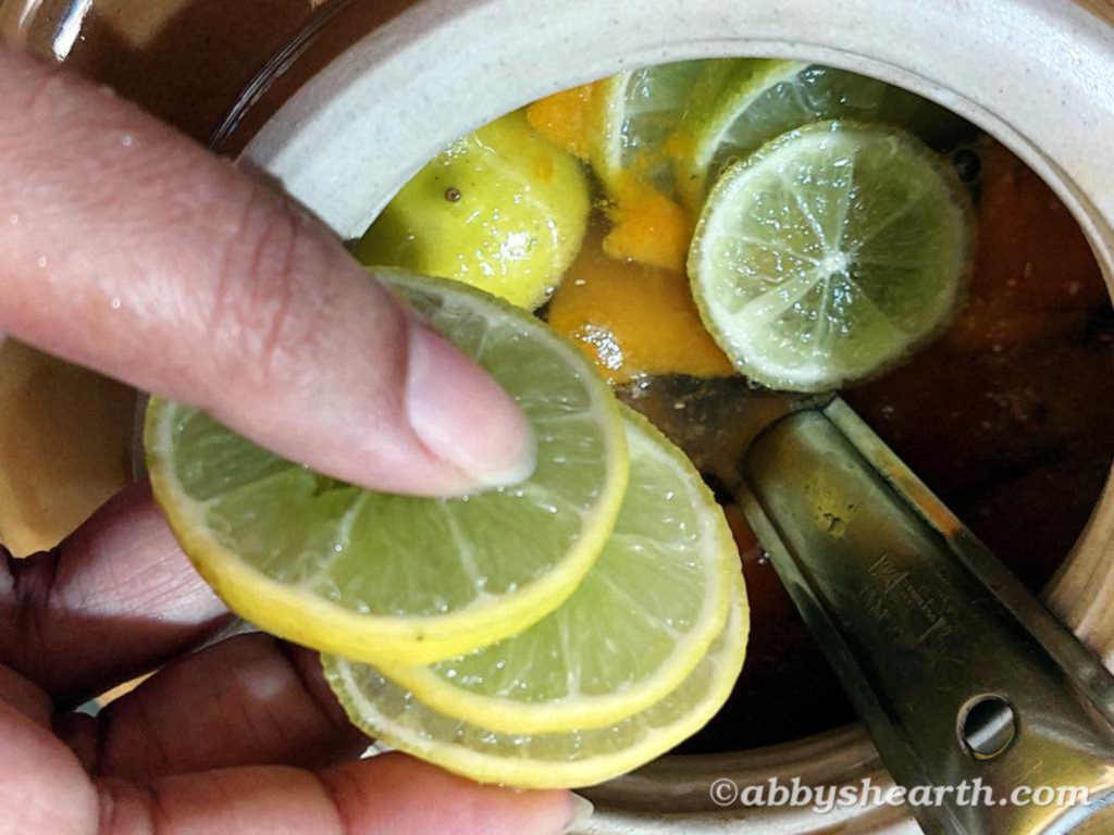 Lemon slices being added to wine must for homemade mango wine fermentation process.