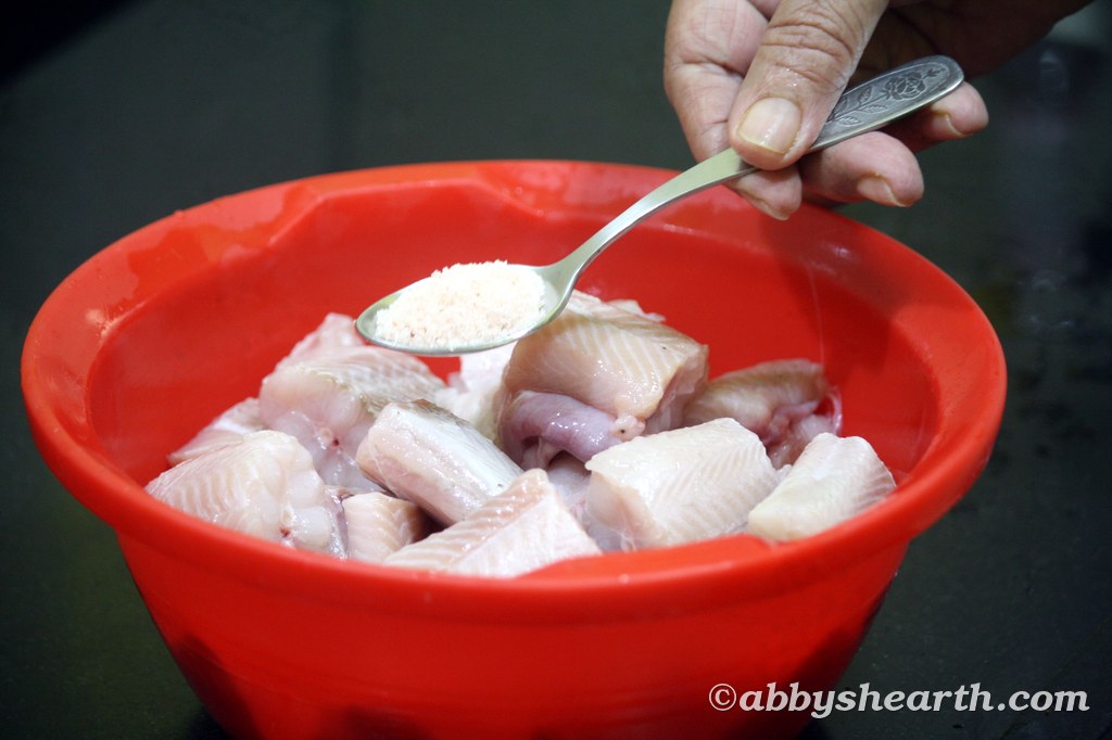 Adding salt to fish pieces in a red bowl.