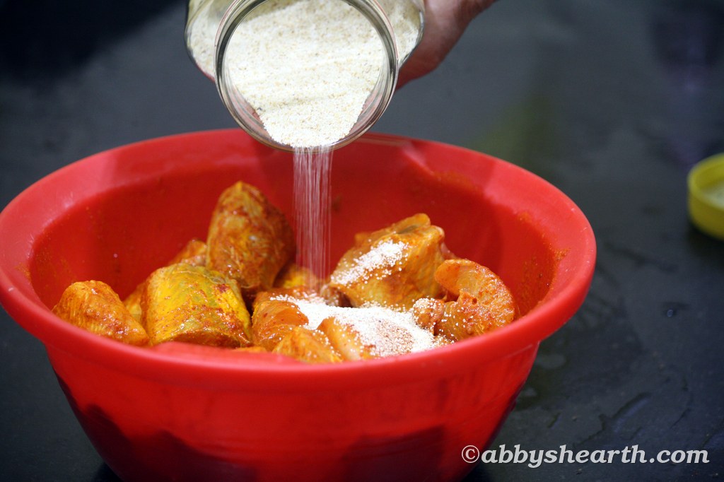 Adding semolina to marinated shark fish in a red bowl.